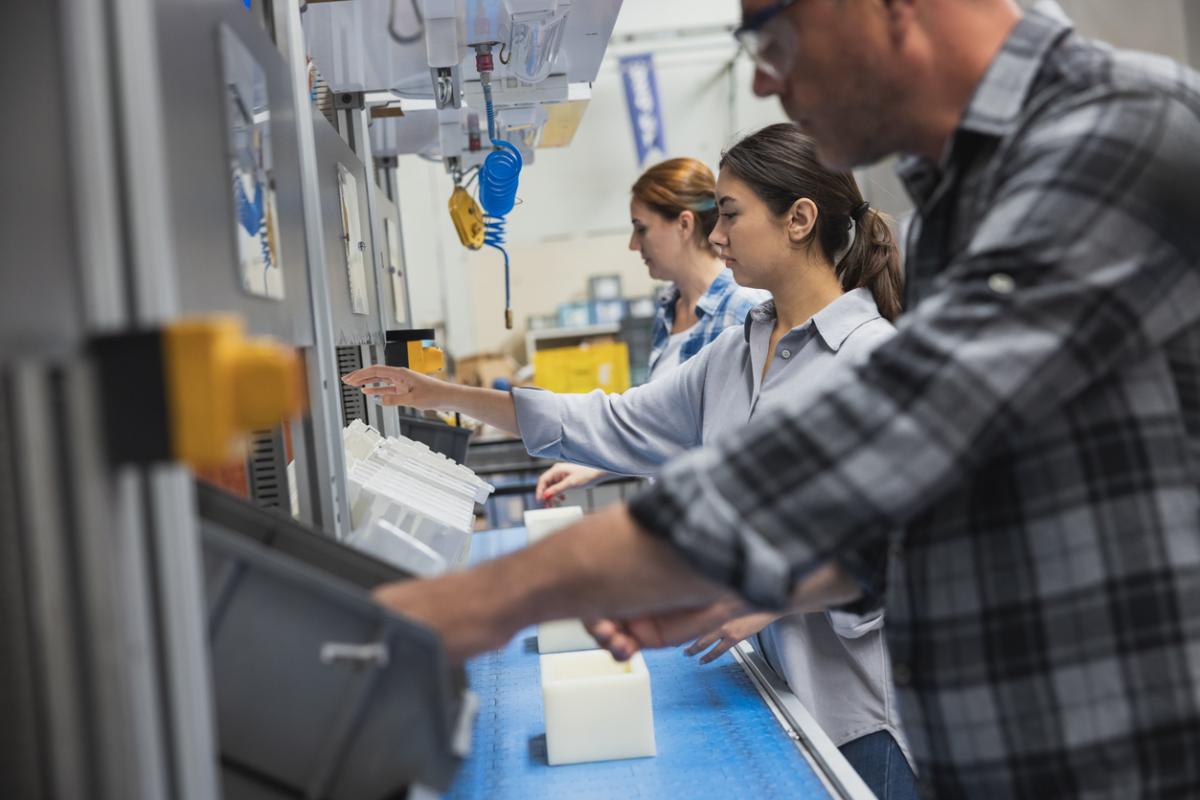 Industrial manufacturing employees lean  over a workstation, performing skilled tasks.