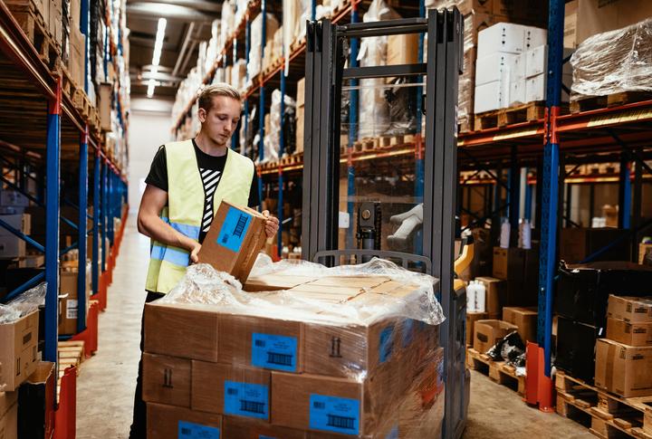 An employee in a hi-vis vest unloads pallets in a warehouse.