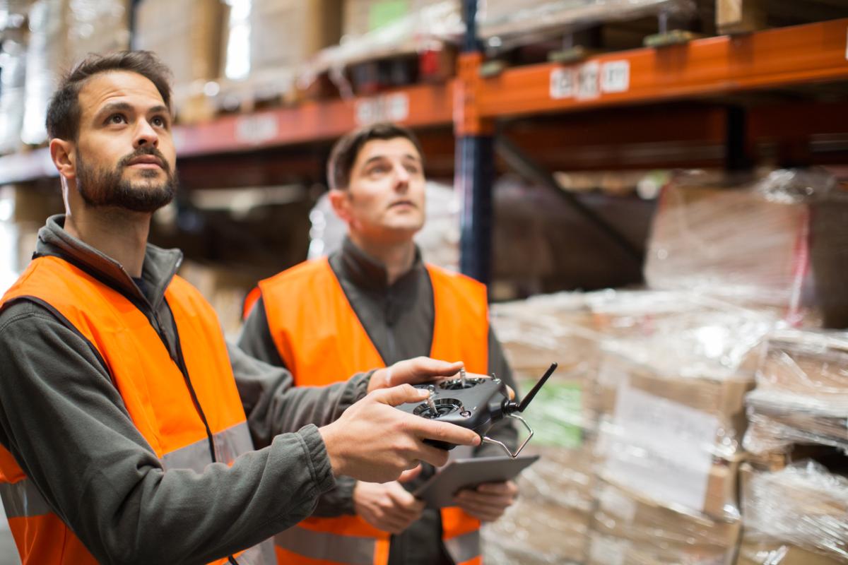 Two workers pilot a drone inside of a warehouse.